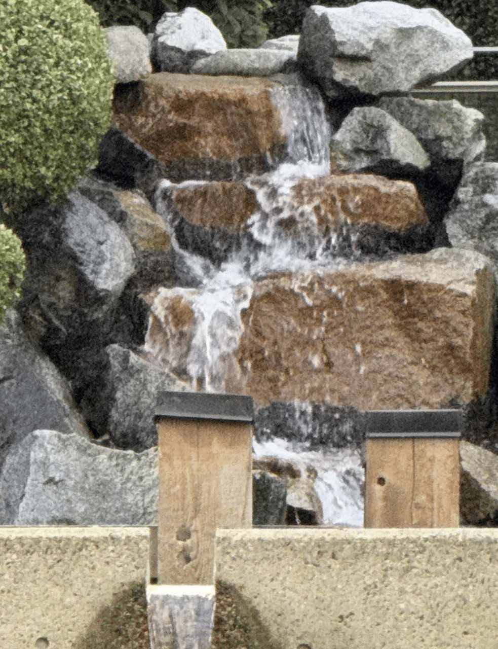 Water tumbling down stacked granite boulders behind two wooden posts