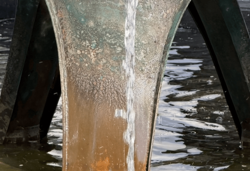 A thin stream of water running down a weathered, flared metal column into a pool